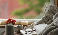 A cup of coffee sits near reading glasses and a book in a cozy nook.