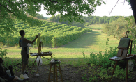 A woman stands before a canvas, painting the grapevines at Parley Lake Winery.