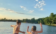 Two kids jumping onto a lily pad float in the lake.