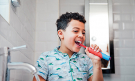 A boy brushes his teeth with an electric toothbrush.