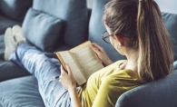 A teenage girl reads a YA novel on her couch.
