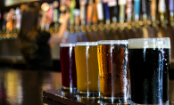 A flight of craft beers sits on a bar. Behind, a row of craft beers on tap.