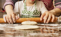 A grandmother helps her granddaughter roll some dough.