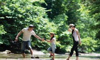 A couple on vacation with their child walks through a river.