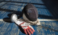 Fencing mask, foil and glove on a blue wood floor.