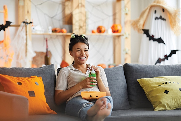 A woman sits on a couch watching scary TV shows.