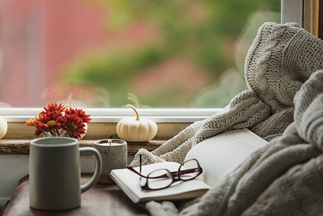 A cup of coffee sits near reading glasses and a book in a cozy nook.