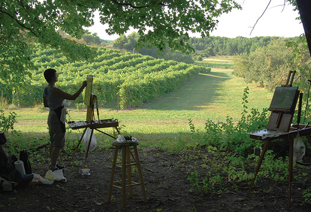 A woman stands before a canvas, painting the grapevines at Parley Lake Winery.