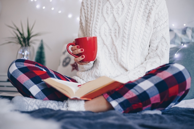 Woman reading and drinking from a red mug.