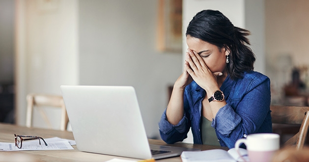 A woman sitting at a computer holds her head in her hands after making a mistake.