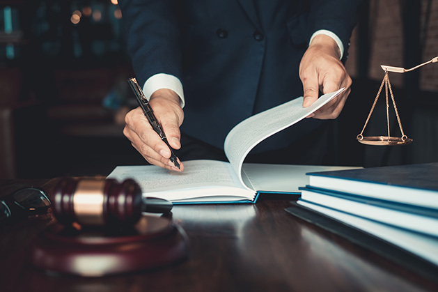 A lawyer writes in a notebook on a desk. A gavel and scales also sit on the desk.