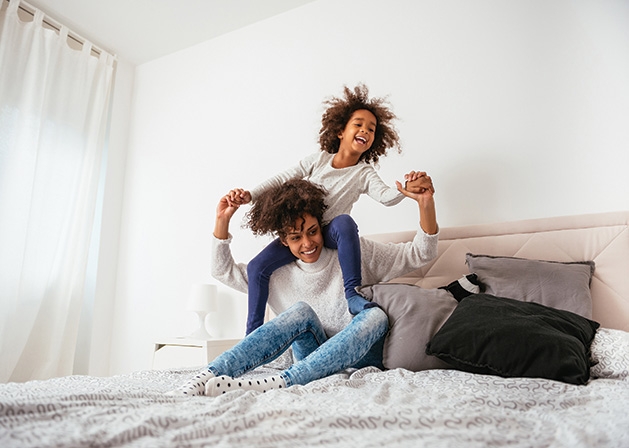 A mother plays with her child on a bed.