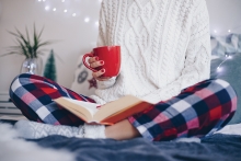 Woman reading and drinking from a red mug.